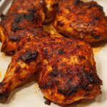 Close-up of juicy Paprika Garlic Baked Chicken Quarters with crispy, charred skin in a white baking dish.