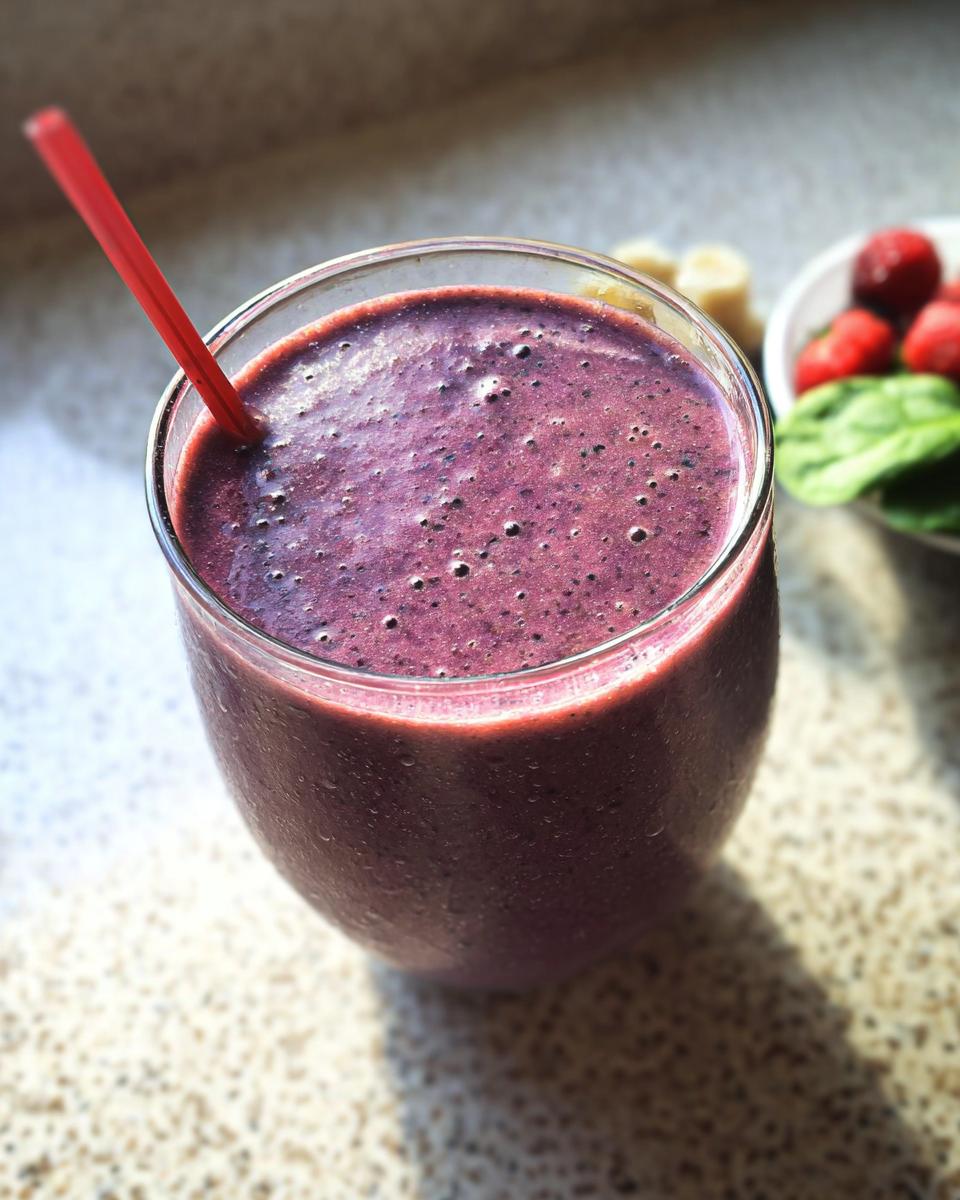 Close-up of a thick, purple berry smoothie in a glass with a red straw, ideal for high-protein smoothies.