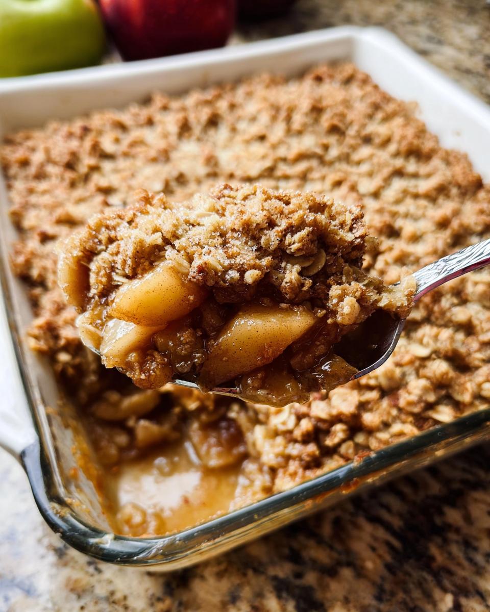 A spoonful of warm Classic Apple Crisp with Oat Crumble showing soft apples and crunchy topping being lifted from a glass baking dish.