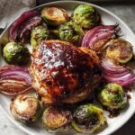 A serving plate featuring Sheet Pan Balsamic Chicken and Brussels Sprouts, glazed and roasted with red onion wedges.