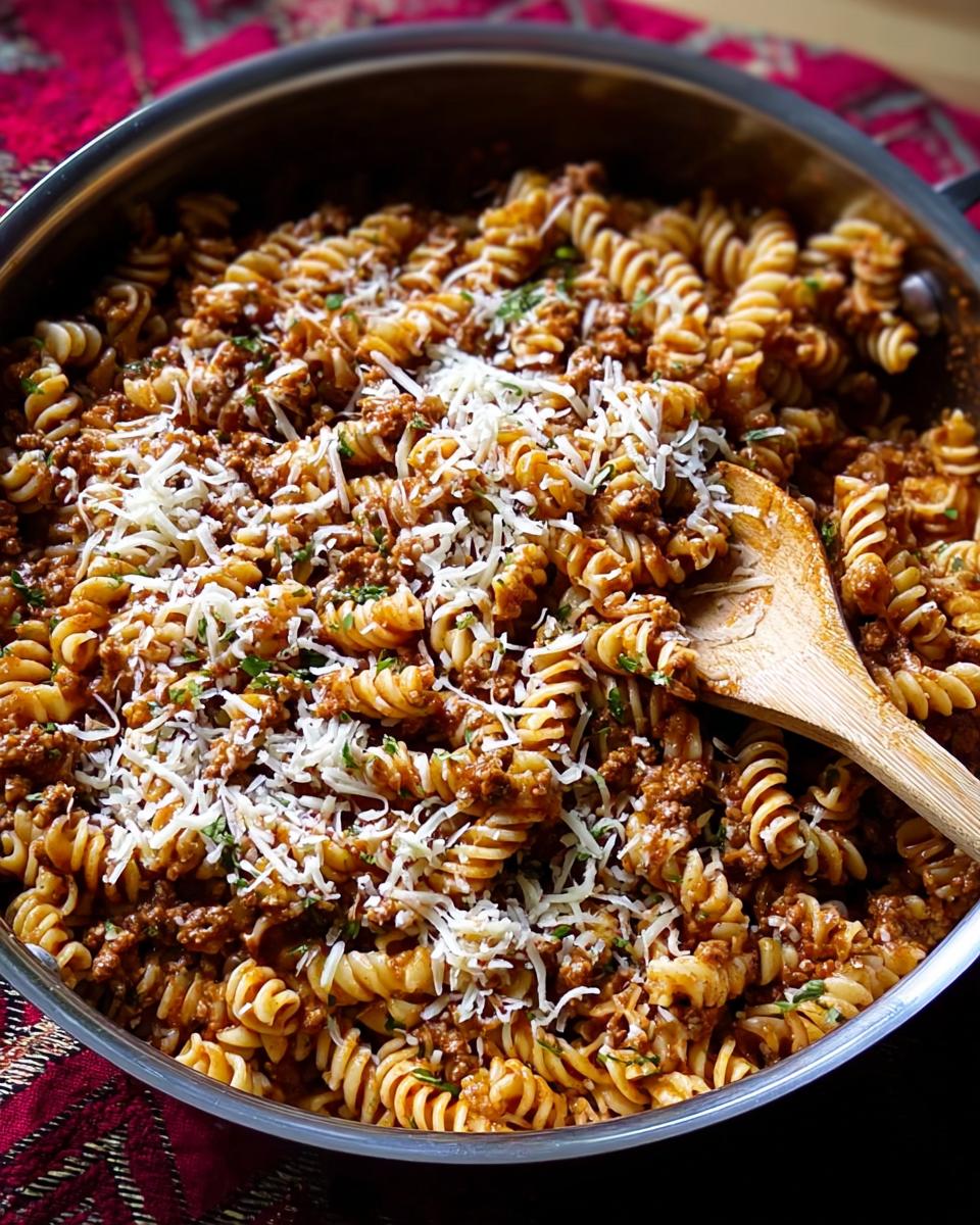 A large skillet filled with rotini pasta coated in a rich sauce and ground turkey, topped generously with shredded cheese.