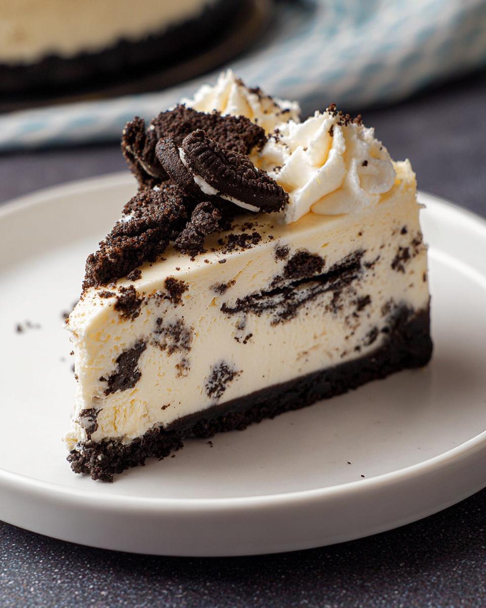 A decadent slice of Oreo Cookies and Cream Cheesecake topped with whipped cream and cookie pieces.