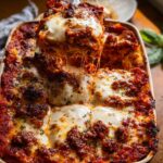 A serving utensil lifts a cheesy slice from a pan of bubbling Spicy Sausage and Ricotta Lasagna, showing long cheese pulls.