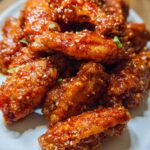 A pile of crispy Sweet Chili Glazed Chicken Wings coated in a shiny, sticky sauce and sprinkled with sesame seeds.