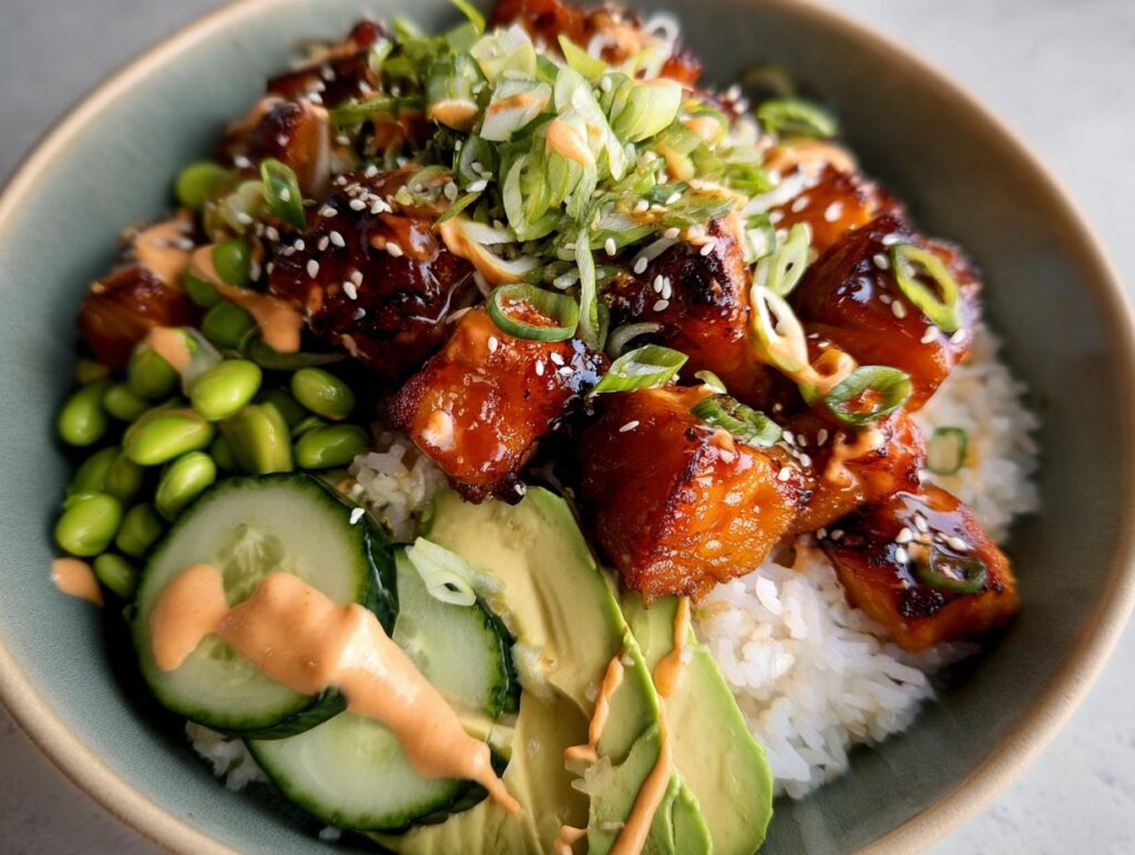 Close-up of Teriyaki Glazed Salmon Rice Bowls featuring glazed salmon cubes over rice with edamame, cucumber, avocado, and spicy mayo.