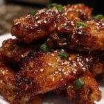 Close-up of sticky, glazed Teriyaki Sesame Baked Chicken Wings topped with white sesame seeds and chopped green onions.