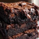 Close-up of three stacked Ultimate Fudgy Dark Chocolate Brownies with melted chocolate chips on top.