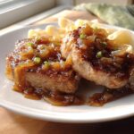 Two seared pork chops topped with rich, caramelized onions, served alongside pasta.