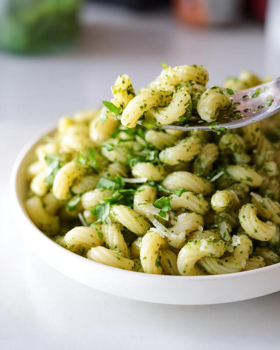 A fork lifting cavatappi pasta coated in bright green pesto sauce, part of our Pasta Recipes in 10 Minutes.
