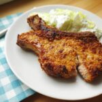 A golden brown, breaded pork chop served on a white plate next to a side of creamy coleslaw, highlighting the crispy texture of the pork chops recipes.