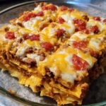 A close-up of a cheesy, layered taco casserole topped with melted cheese and diced tomatoes, perfect for Taco Tuesday recipes.
