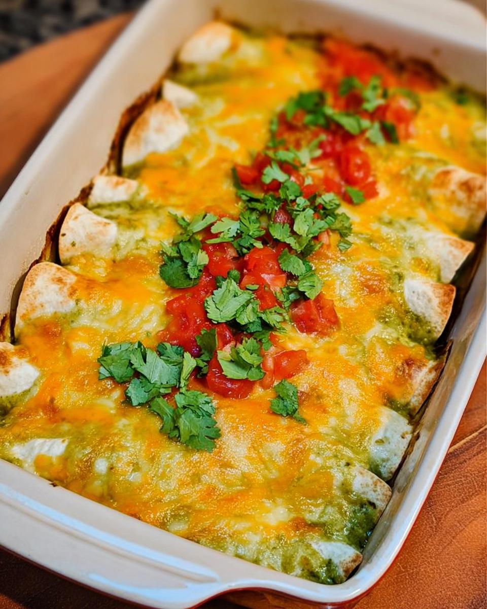Close-up of baked chicken enchiladas verdes topped with melted cheese, diced tomatoes, and cilantro.
