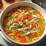 Close-up of a steaming bowl of classic chicken noodle soup recipes, featuring shredded chicken, carrots, and egg noodles.