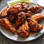 A plate piled high with saucy, glazed chicken wings, served with celery sticks and dipping sauce.
