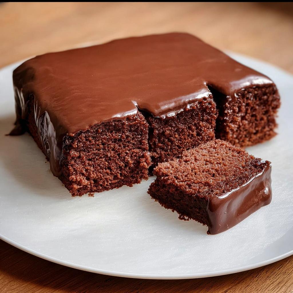 A moist, dark chocolate cake with a thick, glossy chocolate glaze, cut into squares.