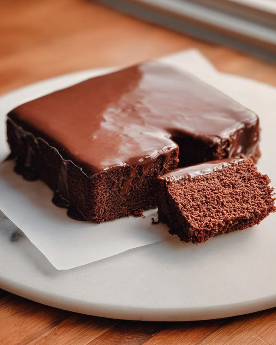 A square slice of rich chocolate cake ideas recipes covered in glossy chocolate ganache, with one piece cut out.