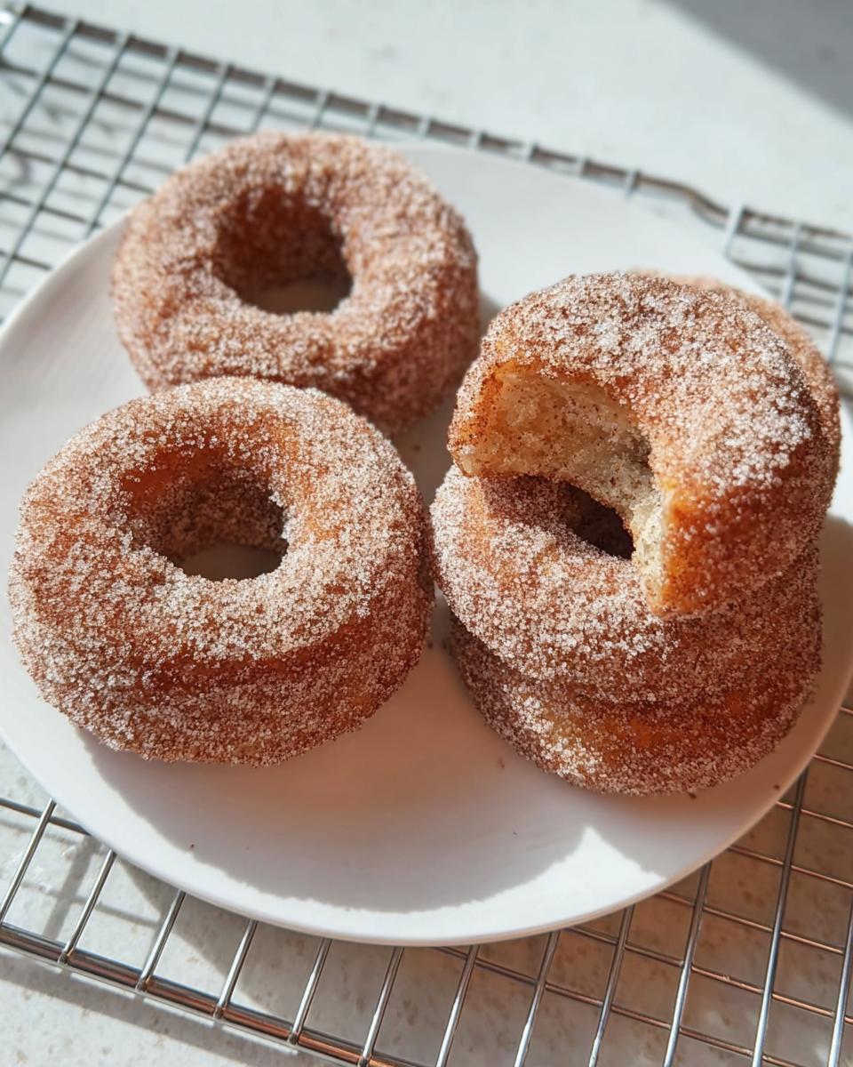 Four homemade cinnamon sugar donuts stacked and placed on a white plate, perfect for breakfast ideas recipes.