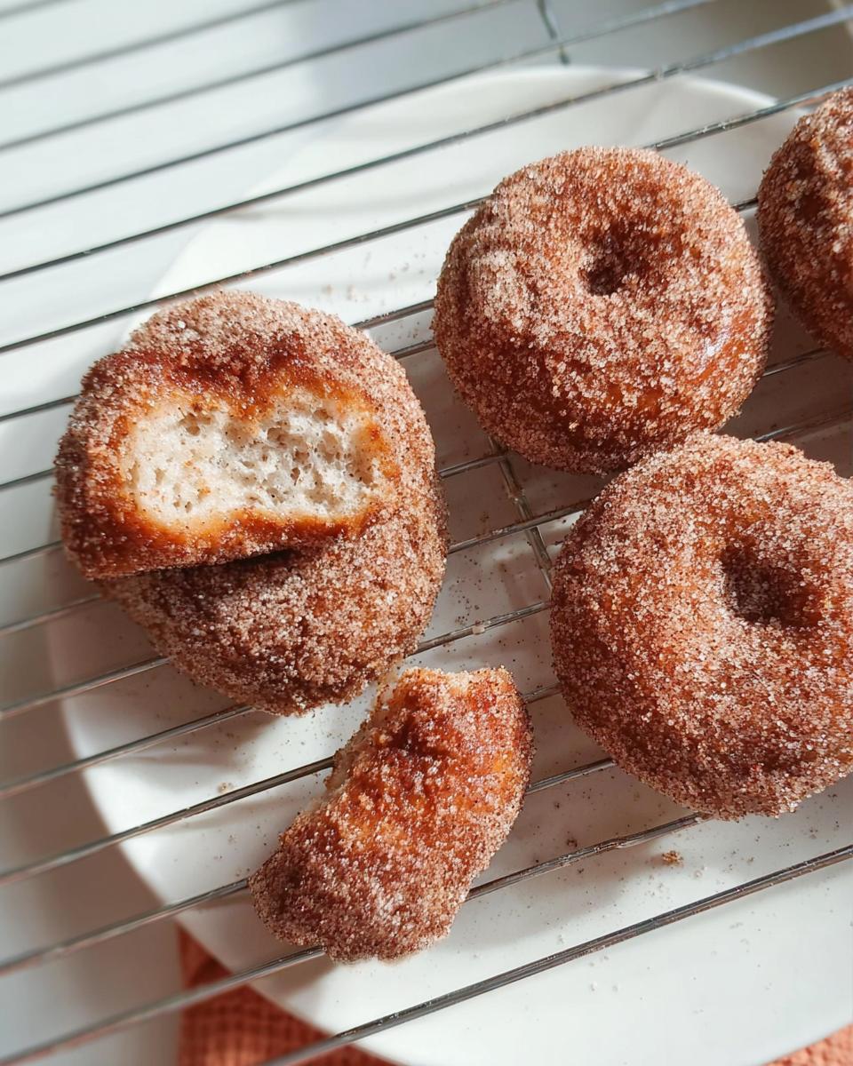 Close-up of fluffy cinnamon sugar donuts cooling on a wire rack, one donut is broken open.