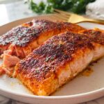 Two perfectly seasoned and cooked salmon fillets on a white plate, showcasing flaky texture, a key element in great salmon recipes.