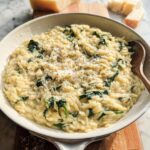 A bowl of creamy orzo pasta mixed with wilted spinach and topped with grated Parmesan cheese, a perfect veggie sides recipe.