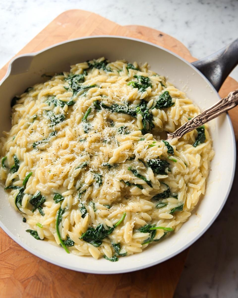 Creamy spinach orzo pasta topped with grated Parmesan cheese, served in a white skillet.