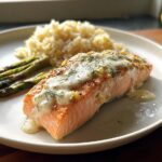 Pan-seared salmon fillet topped with creamy dill sauce, served with rice and grilled asparagus.