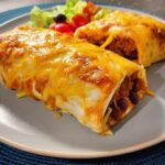 Two baked burritos covered in melted cheddar cheese served with a side salad, perfect for easy dinner recipes.