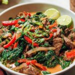 A vibrant bowl of easy beef and spinach curry with red peppers and lime wedges.