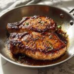Two beautifully seared, glazed pork chops resting in a stainless steel skillet with pan juices, perfect for Pork Chops Recipes Meal Prep.