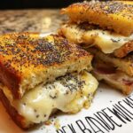 Close-up of two halves of a gourmet grilled cheese sandwich with melted cheese and poppy seeds.