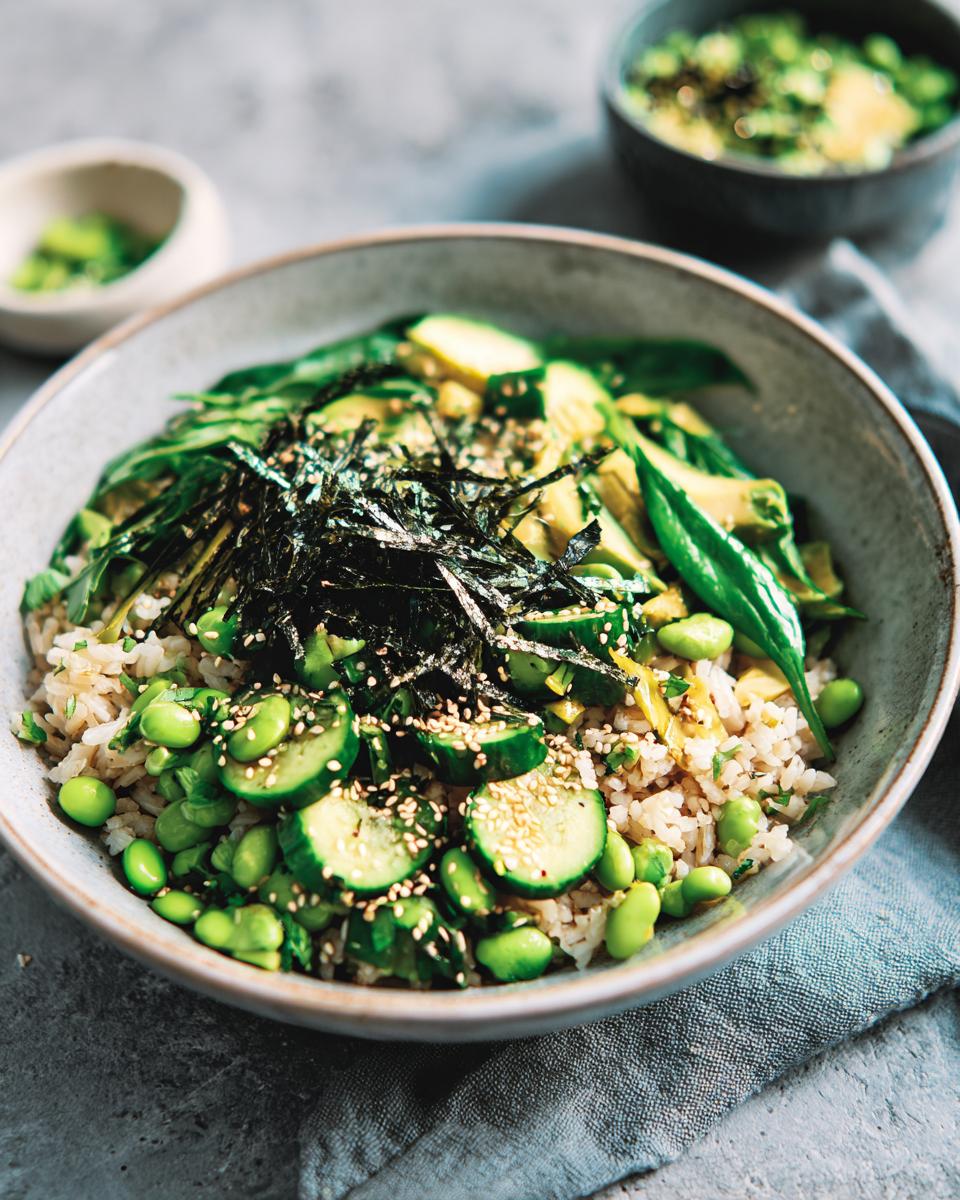 A vibrant green vegetarian rice bowl featuring brown rice, edamame, cucumber, avocado, and nori strips.