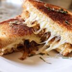 A perfectly grilled cheese recipe featuring melted, stringy cheese and caramelized onions, garnished with thyme.