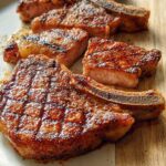 Four perfectly seared, thick-cut bone-in pork chops resting on a wooden board, showing a beautiful crust.