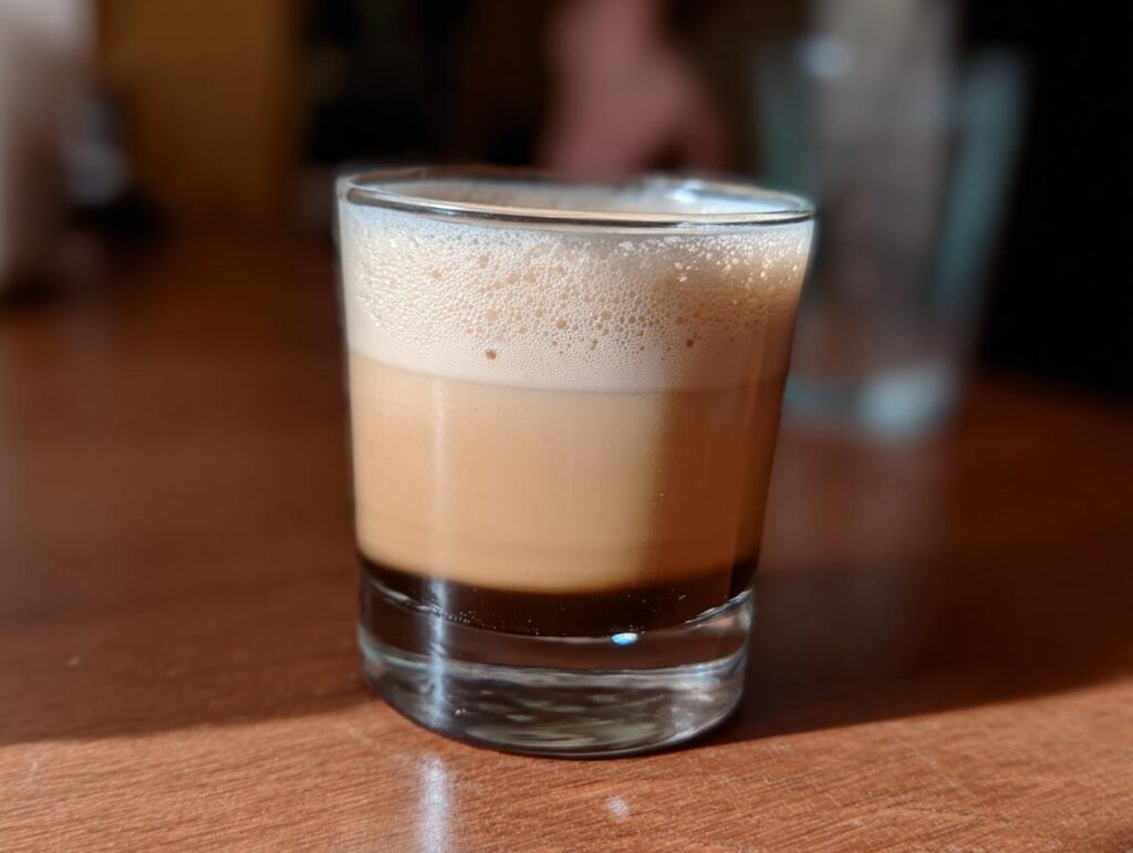 A small glass containing a layered coffee drink, likely an espresso shot with milk and foam, part of Starbucks Drinks Recipes Ideas.