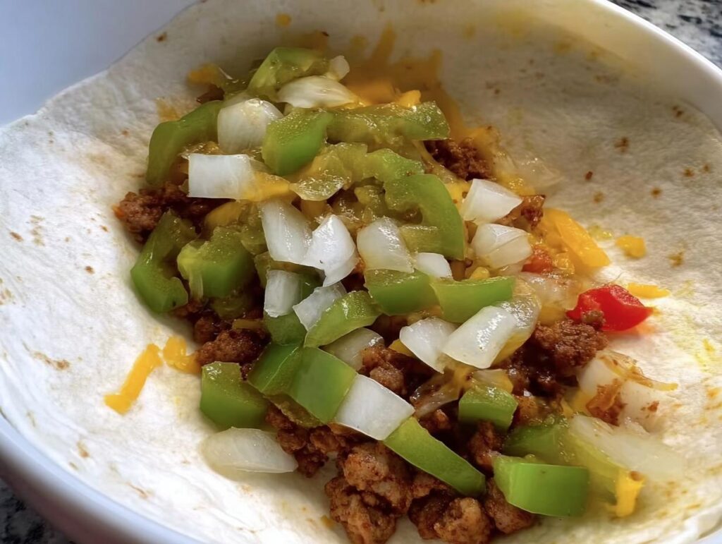 Close-up of a tortilla filled with seasoned ground meat, diced green peppers, onions, and shredded cheese, part of an egg recipe.