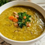 Close-up of thick, green split pea soup topped with ham, carrots, parsley, and black pepper, demonstrating how to make soup recipes.