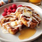 Two decadent cinnamon rolls drizzled with icing, butter, and syrup, served with fresh raspberries for Restaurant-Style Breakfast Ideas.