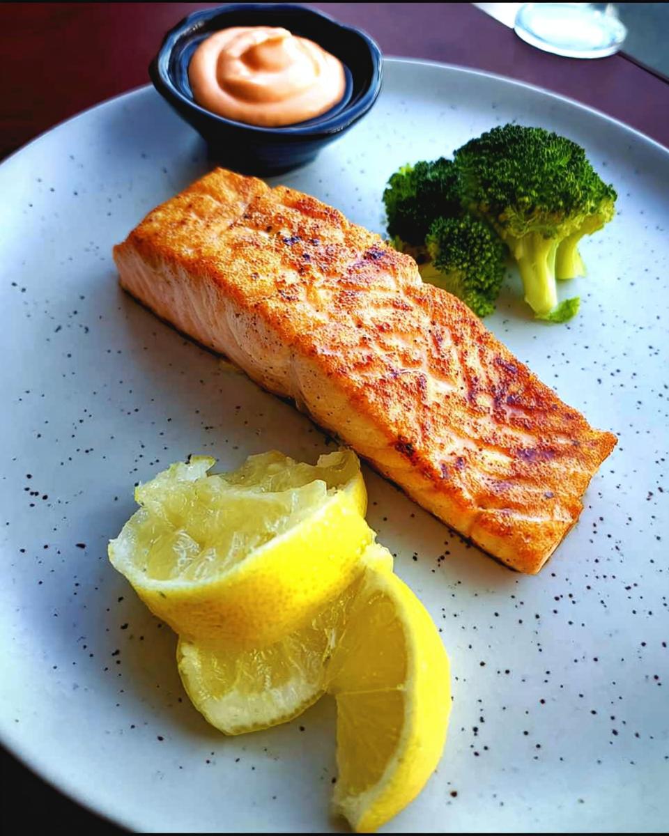 A perfectly cooked salmon fillet served with lemon wedges, broccoli, and a side of pink sauce, illustrating 12-Ingredient Salmon Recipes.