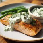 A perfectly cooked salmon fillet topped with creamy dill sauce, served with green beans.