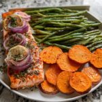 A perfectly cooked salmon fillet topped with red onion and lemon slices, served alongside roasted sweet potato rounds and green beans, ideal for salmon recipes meal prep.