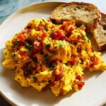Fluffy scrambled eggs mixed with diced red tomatoes and fresh herbs, served with toasted bread. A perfect example of Egg Recipes in 10 Minutes.