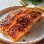 Two perfectly cooked, spice-rubbed salmon fillets served on a speckled white plate, part of The Ultimate Salmon Recipes Guide for Beginners.