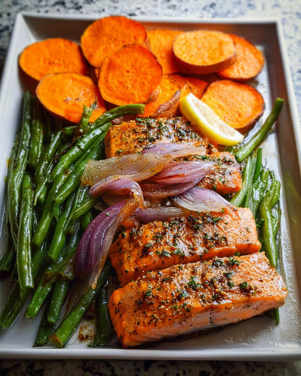 Three pieces of seasoned salmon served with roasted green beans, sweet potato slices, and red onion for Salmon Recipes Meal Prep.