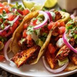 Close-up of three seasoned chicken tacos topped with salsa, red onion, and crema, perfect for Taco Tuesday Recipes Meal Prep.