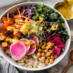 Overhead view of a colorful, healthy rice bowls recipe featuring brown rice, roasted sweet potatoes, kale, and bright pink radishes.