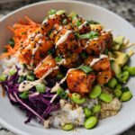 A vibrant bowl featuring crispy Bang Bang Salmon Bites served over rice and quinoa with shredded red cabbage, carrots, edamame, and avocado.