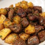 A close-up of glistening, pan-seared garlic steak bites mixed with golden roasted potatoes.