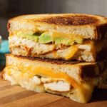 A stacked, halved Chicken Avocado Melt Sandwich showing melted cheese, chicken, and avocado slices between grilled bread.