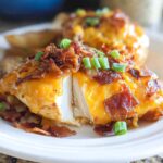 A serving of Cowboy BBQ Bacon Cheddar Chicken, sliced to show the white meat, topped with melted cheddar and crispy bacon bits.