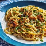 A close-up of creamy Cowboy Butter Chicken Pasta topped with fresh parsley on a white and blue plate.